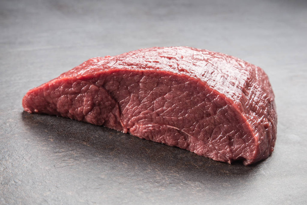 Portion of raw beef thigh on dark butcher board. - Фото, изображение