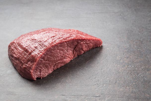 Portion of raw beef thigh on dark butcher board. - Zdjęcie, obraz