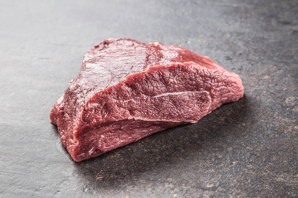 Portion of raw beef shoulder on dark butcher board. - 写真・画像