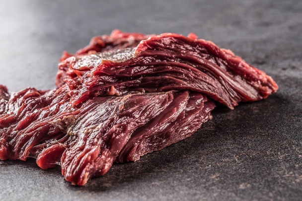 Portion of raw beef meat on dark butcher board. - 写真・画像