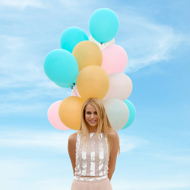 Retrato de una joven feliz con un montón de globos contra el cielo azul
 - Foto, imagen