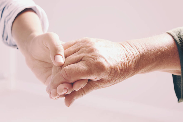 Woman holding hands with senior lady on light background, closeup. Elderly care and help concept - Φωτογραφία, εικόνα
