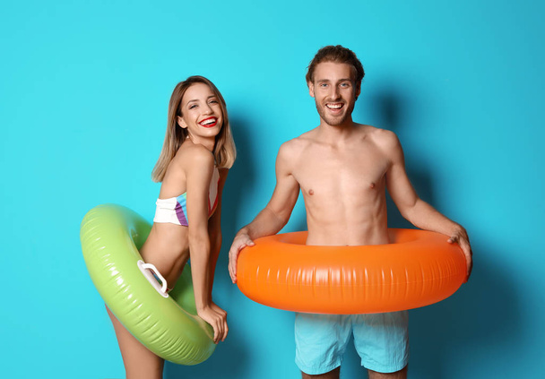 Happy young couple in beachwear with inflatable rings on color background - Foto, Bild