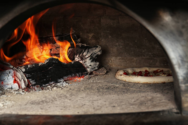 Oven with burning firewood and tasty pizza in restaurant kitchen - Foto, Imagem