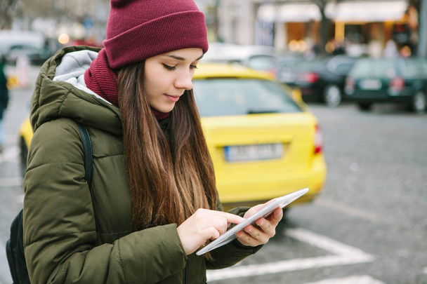 Egy tabletta, egy utcában, Prága gyönyörű turista lány hív egy taxit úgy néz ki, egy térképen, vagy használja az interneten, vagy egy mobil alkalmazás. - Fotó, kép