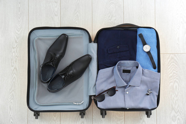 Open suitcase with clothing, shoes and accessories on wooden background - Foto, Bild