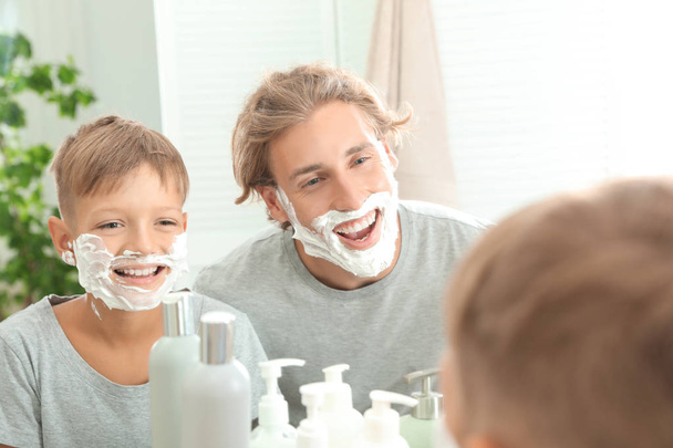 Father and son with shaving foam on faces in bathroom - 写真・画像