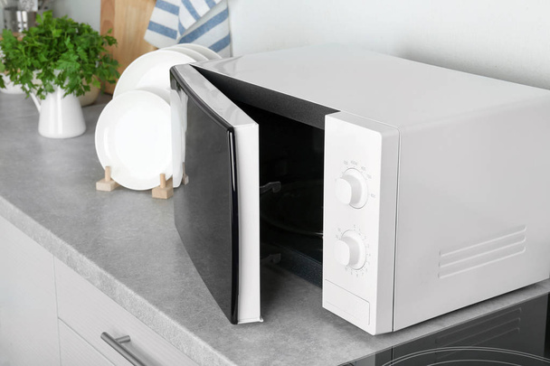 Open modern microwave oven on table in kitchen - Фото, изображение
