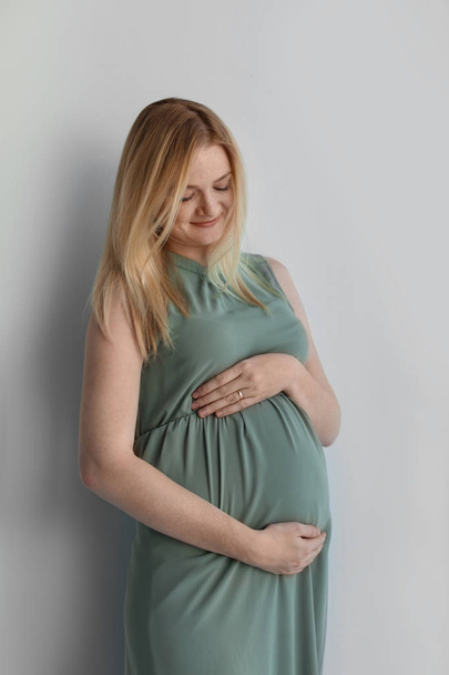 Jovem grávida tocando barriga no fundo claro
 - Foto, Imagem