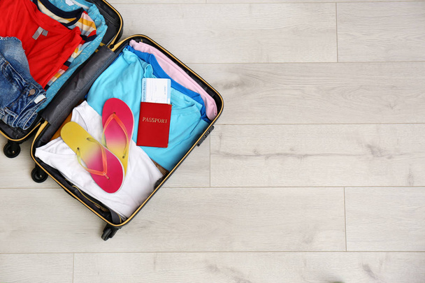 Packed suitcase with summer clothes and passport on wooden background, top view. Space for text - Foto, imagen