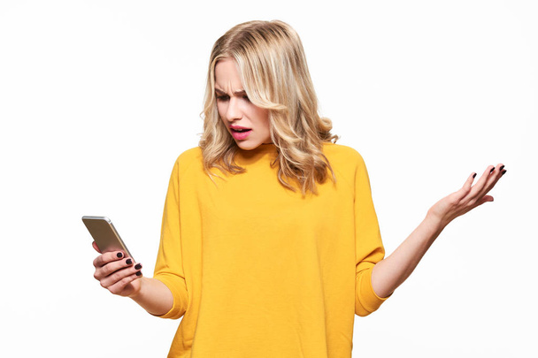 Shocked angry young woman looking at her mobile phone in disbelief. Woman staring at shocking text message on her phone, isolated over white background. - 写真・画像
