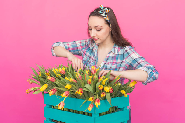 Boldog kaukázusi fiatal nő doboz rózsaszín háttér sárga tulipánok - Fotó, kép