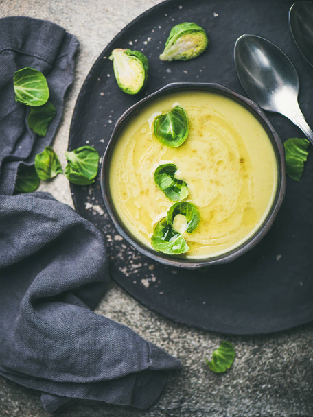 Seasonal brussels sprouts vegetable cream soup in black bowl and fresh green brussel sprouts over black plate, top view. Vegan, vegetarian, healthy, dieting food concept - Fotoğraf, Görsel