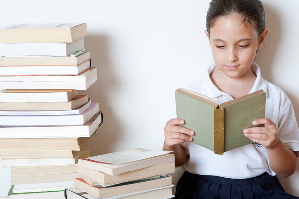 junges Mädchen liest zu Hause ein Buch, umgeben von Bücherstapeln. - Foto, Bild