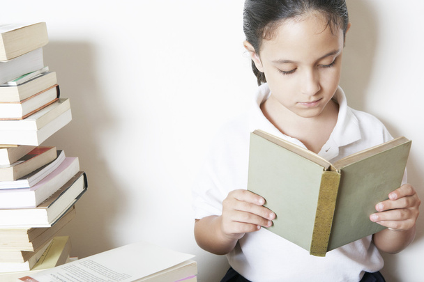 ながら、本を自宅での杭の横に座って本を読んで若い学校の女の子. - 写真・画像