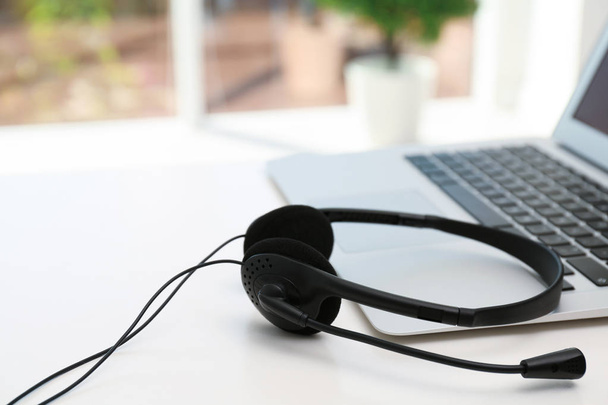 Modern laptop and headset on table indoors. Technical support concept - 写真・画像