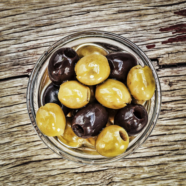 Olives close up, top view. Black and green olives in a glass bowl on a wooden background - Photo, Image