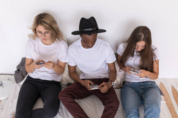 Multiracial group of friends are sitting on the bed and usie smartphone. - Foto, Imagen