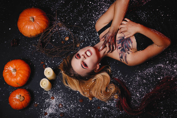 Halloween käsite, tyttö vampyyri punaiset silmät punaiset huulet makaa lattialla kurpitsat ja lunta ympärillä. Pelottava hullu nainen karkki tai kepponen. Nainen meikki loma kynttilä
 - Valokuva, kuva