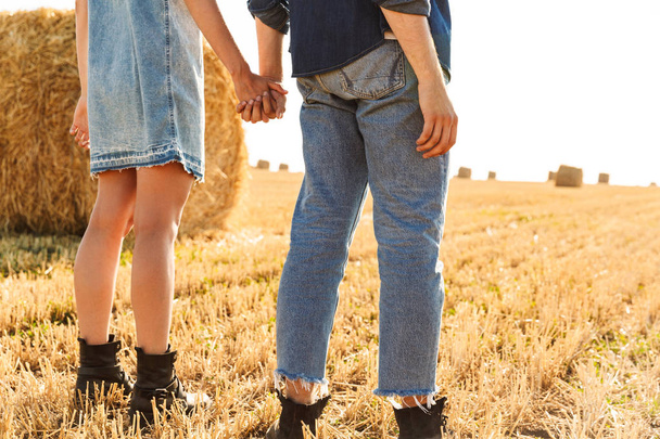 Back view cropped image of a young couple standing together at the wheat field, holding hands - Fotografie, Obrázek