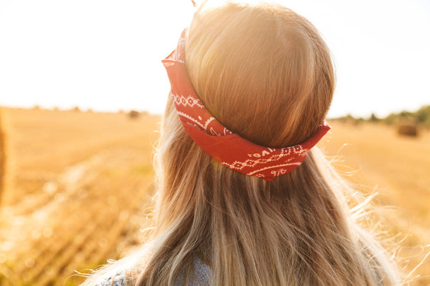 Back view of a young blonde girl in headband at the wheat field looking away - Foto, Imagem