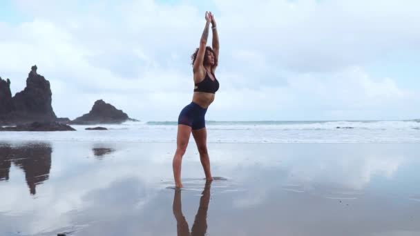 the girl does a warm-up before doing sports early in the morning on the seashore. A girl of athletic build with a dry muscle mass. - Footage, Video