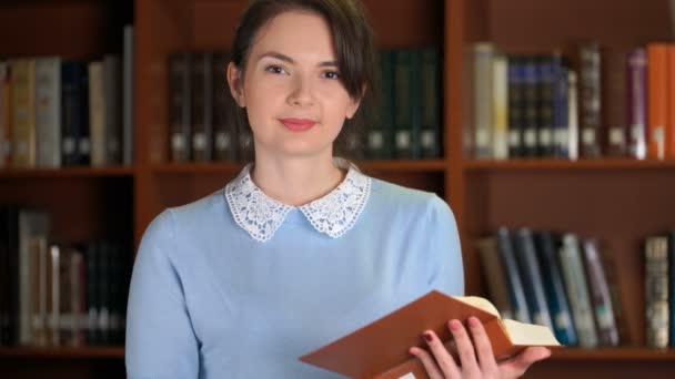 Porträt einer lächelnden schönen Frau mit Buch im Bücherregal der Bibliothek - Filmmaterial, Video