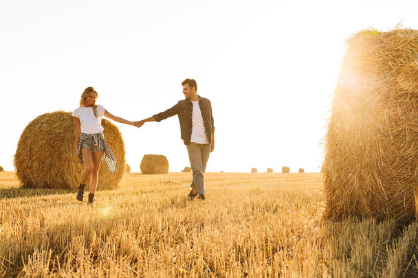 Photo of amazing people man and woman walking through golden field with bunch of haystacks during sunny day - Φωτογραφία, εικόνα