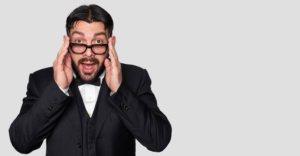 Surprised bearded man in tuxedo and eyeglasses isolated on grey background - Foto, Imagen