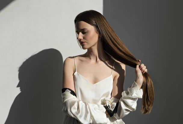 молода брюнетка жінка тримає довге блискуче волосся
  - Фото, зображення