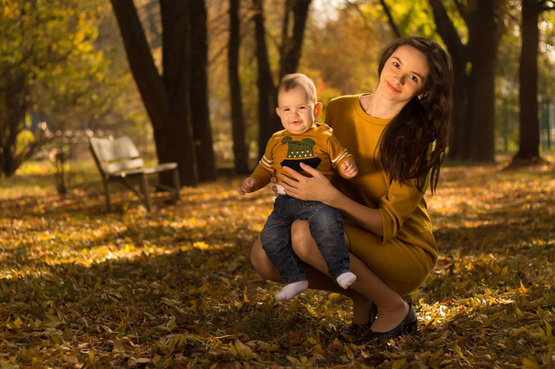 Happy young mother playing with baby in autumn park with yellow maple leaves.Family walking outdoors in autumn. Little boy with her mother playing in the park in autumn. - Photo, Image