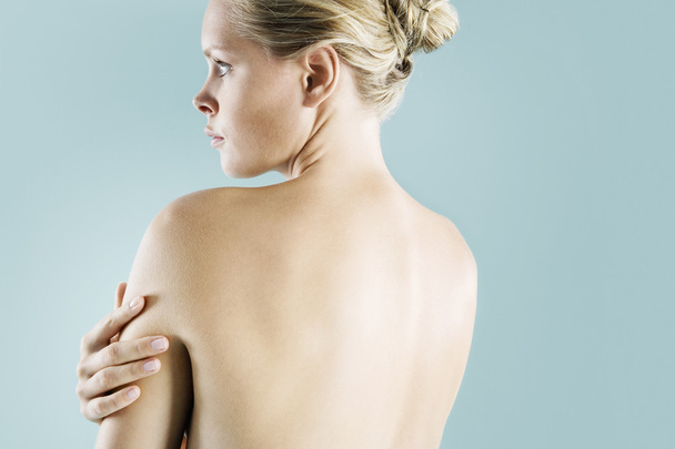 Vista posteriore di una donna bionda nuda che guarda avanti su uno sfondo blu
. - Foto, immagini