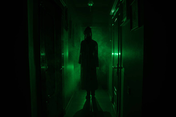 Creepy sylwetka w ciemny budynek opuszczony. Koncepcja Halloween horror. Ciemny korytarz z sylwetka osoby horror, stojący w centrum. Kontrasty światła i mgła na tle. - Zdjęcie, obraz