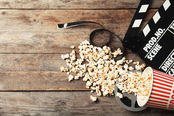 Tasty popcorn, film reel and clapperboard on wooden background, top view with space for text. Cinema snack - Foto, afbeelding