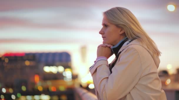 Μια νεαρή γυναίκα στέκεται κλίνει σχετικά με την κουπαστή της γέφυρας, θαυμάζοντας το υπέροχο ηλιοβασίλεμα. - Πλάνα, βίντεο