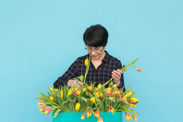 Middle-aged woman florist with wooden box of tulips on blue background - Photo, Image