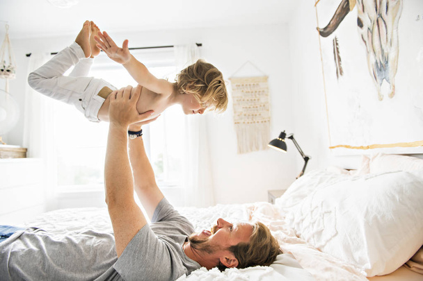 Happy father playing with his boy on a bed at home - Foto, Imagem