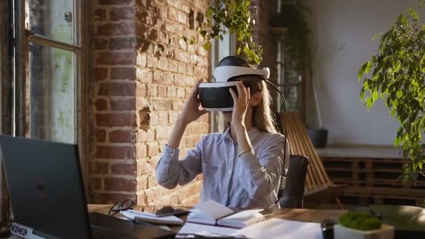 Young creative girl uses virtual reality glasses at workplace in modern office at the evening. Beautiful girl r uses virtual reality glasses - Filmati, video