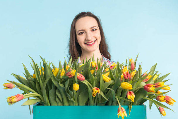 Белая молодая женщина с большой связкой тюльпанов на синем фоне
 - Фото, изображение
