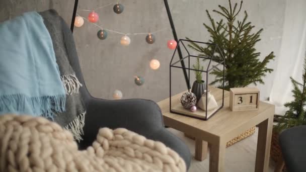 Κομψό Χριστούγεννα Σκανδιναβικές εσωτερικό με μια κομψή πολυθρόνα και ζεστή merinos καρό. Άνεση σπίτι με Σκανδιναβική νέο έτος διακόσμηση. Μίνιμαλ χριστουγεννιάτικο δέντρο με γιρλάντες και τα φώτα στο φως του δωματίου. - Πλάνα, βίντεο