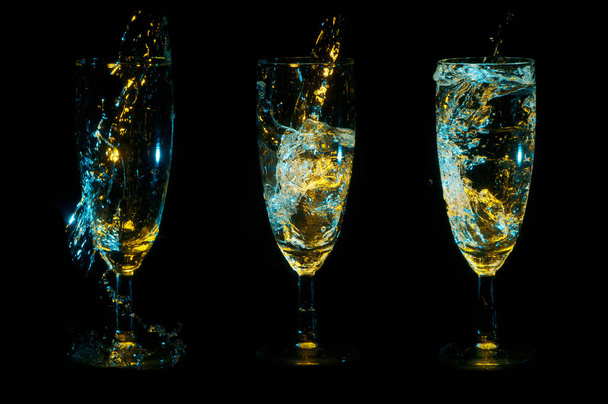 徐々 に黒の背景上の透明な液体で満たされているブルーとゴールドのライトの下で 3 つのグラス - 写真・画像