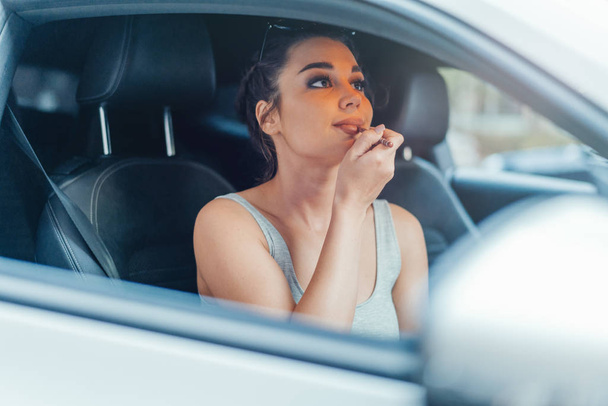 Close up of beautiful woman getting her lips painted while sitting in car. - Photo, image