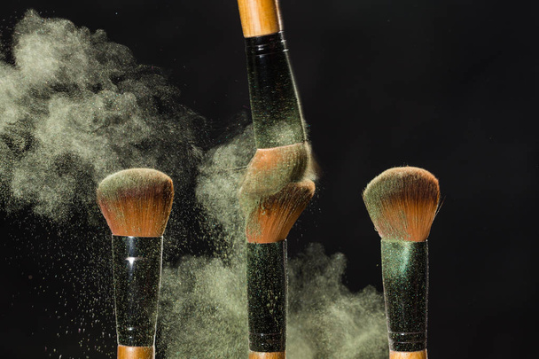Make up, beauty and mineral powder concept - Cosmetics brush and explosion colorful makeup powder background - Photo, Image