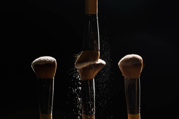 Cosmetic brush with cosmetic powder spreading on black background - Foto, Imagen