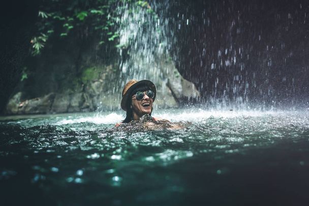 Happy young woman tourist swimming in the deep jungle with waterfall. Real adventure concept. Bali island. - Photo, Image