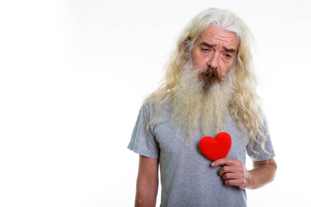 Studio shot of senior bearded man holding red heart while lookin - Foto, afbeelding