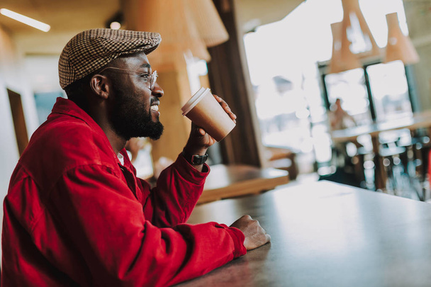 Young man looking glad while sitting alone and drinking coffee - Photo, Image