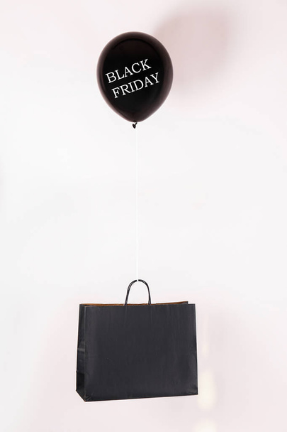 Black friday text on flying balloon lifting shopping bag. Fourth Friday of November, beginning of Christmas shopping season since 1952. Copy space, close up, top view, flat lay, background. - Photo, Image