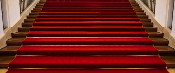 Vörös szőnyegen luxus. Fa lépcsők a bolzákon borított vörös szőnyegen háttér, perspektivikus nézet - Fotó, kép