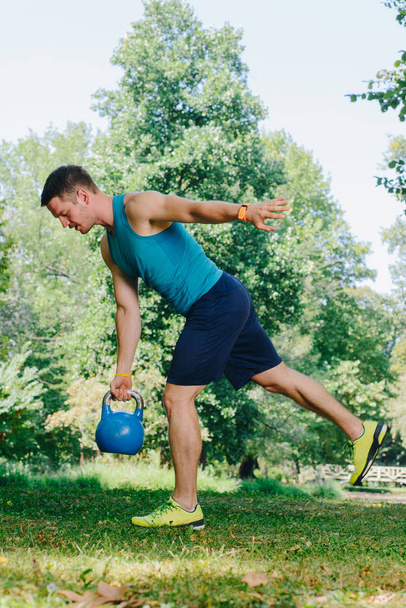 Aantrekkelijke fitness instructeur doen zwaar gewicht oefening met de kettlebell in het park - Foto, afbeelding